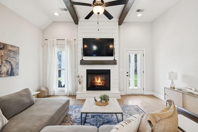 living room with visible vents, beamed ceiling, a fireplace, ceiling fan, and wood finished floors