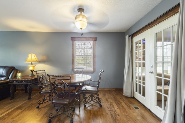 dining area with a textured ceiling, visible vents, wood finished floors, french doors, and baseboards