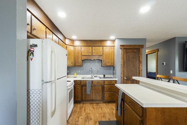 kitchen with white appliances, light wood-type flooring, light countertops, a sink, and brown cabinets