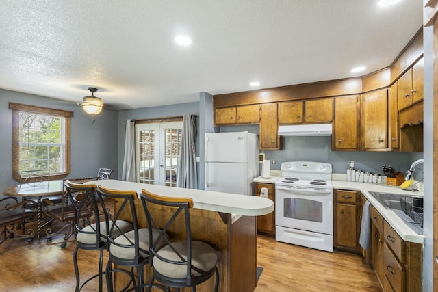 kitchen with a sink, light countertops, white appliances, under cabinet range hood, and brown cabinetry