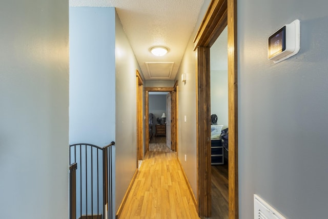 corridor with light wood-style flooring, a textured ceiling, and baseboards