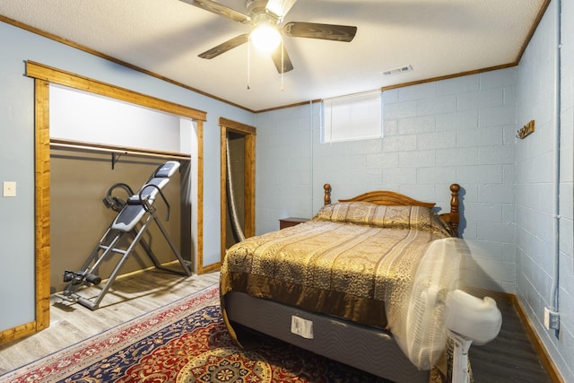 bedroom with wood finished floors, ornamental molding, visible vents, and concrete block wall