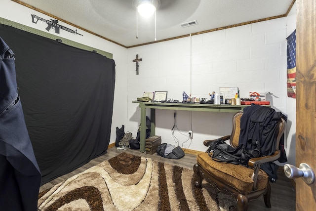interior space featuring visible vents, a ceiling fan, a textured ceiling, concrete block wall, and wood finished floors
