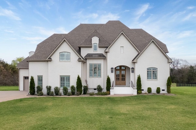 french country inspired facade featuring french doors, concrete driveway, roof with shingles, an attached garage, and a front lawn