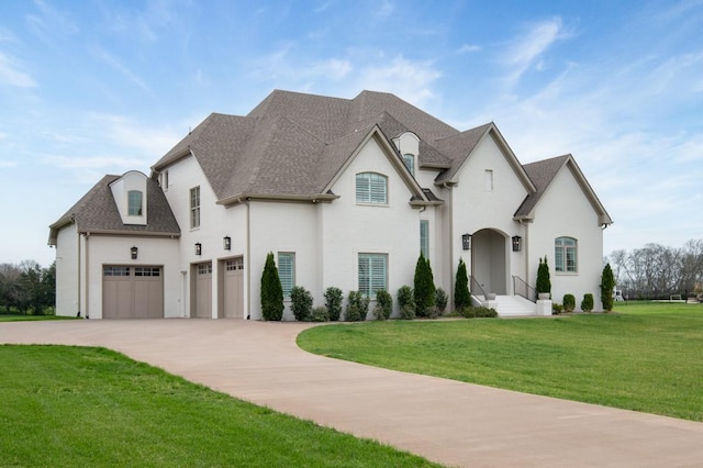 french country inspired facade with a front yard, concrete driveway, stucco siding, a shingled roof, and a garage