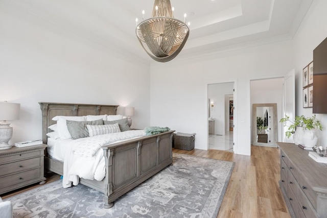 bedroom with a tray ceiling, a notable chandelier, a high ceiling, ensuite bathroom, and light wood-style floors