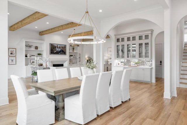 dining space with arched walkways, light wood-style floors, beamed ceiling, and stairs