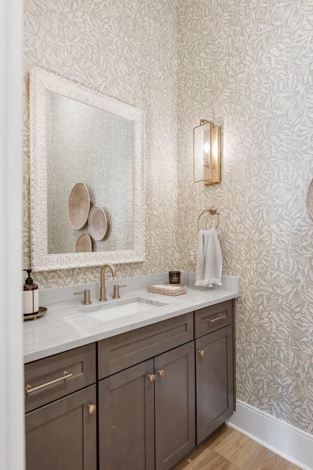 bathroom featuring baseboards, wallpapered walls, wood finished floors, and vanity