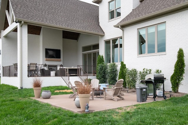 back of property with a lawn, brick siding, roof with shingles, and a patio area
