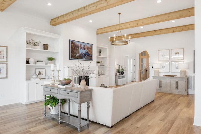 living area with light wood-style flooring, built in shelves, beam ceiling, arched walkways, and a notable chandelier