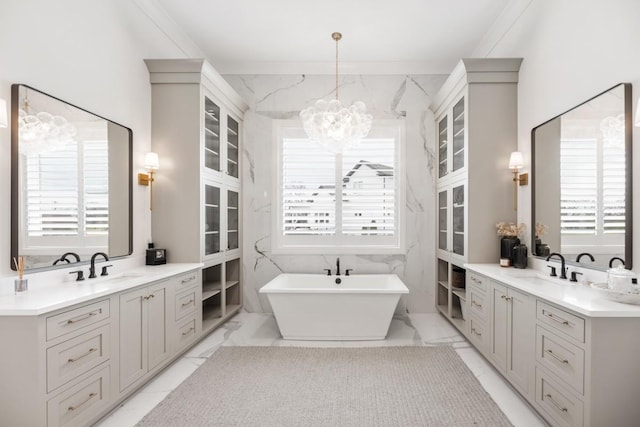 full bathroom with marble finish floor, a freestanding tub, two vanities, a sink, and an inviting chandelier