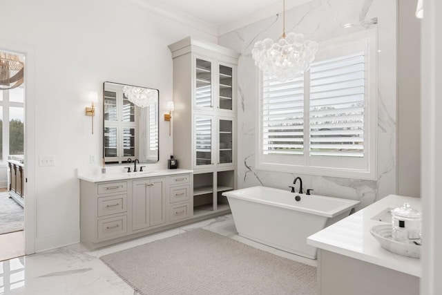full bath with a chandelier, marble finish floor, ornamental molding, vanity, and a freestanding bath