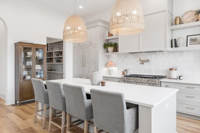kitchen with open shelves, a chandelier, decorative backsplash, range, and light wood-style floors