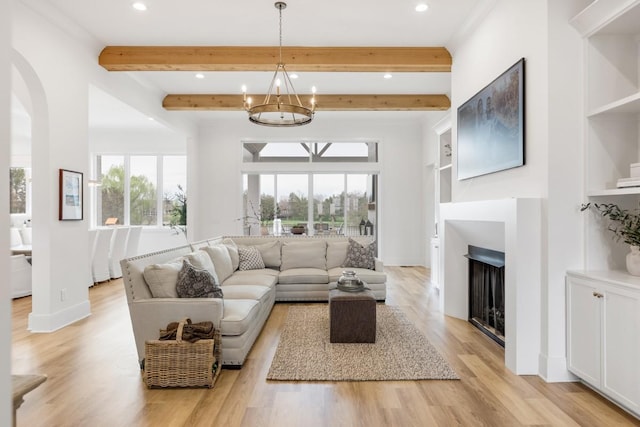 living room featuring beam ceiling, a fireplace, light wood-type flooring, baseboards, and an inviting chandelier