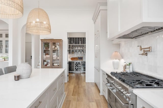 kitchen with range with two ovens, light countertops, tasteful backsplash, light wood-type flooring, and arched walkways