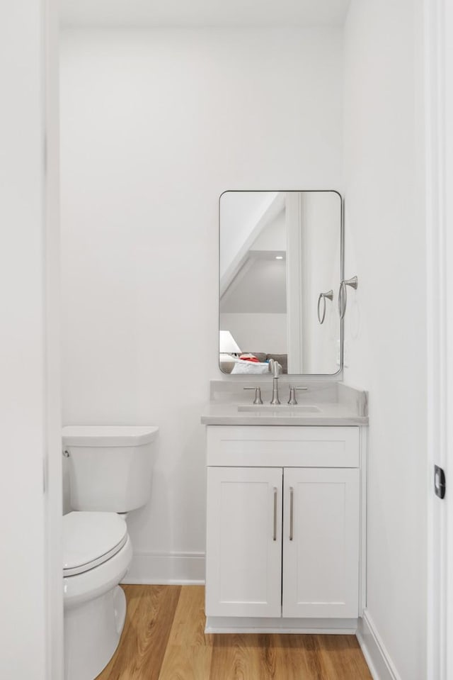 half bath with baseboards, toilet, wood finished floors, and vanity