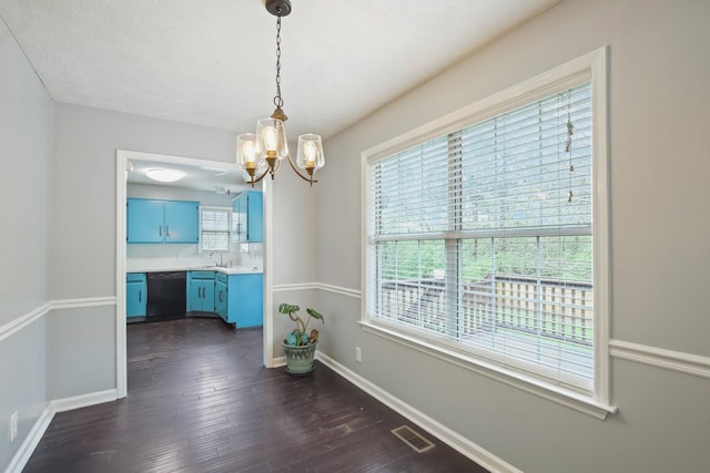 unfurnished dining area featuring an inviting chandelier, a sink, dark wood-type flooring, and a healthy amount of sunlight