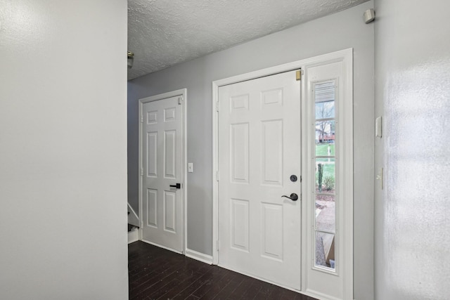 foyer entrance featuring baseboards, a textured ceiling, and dark wood finished floors