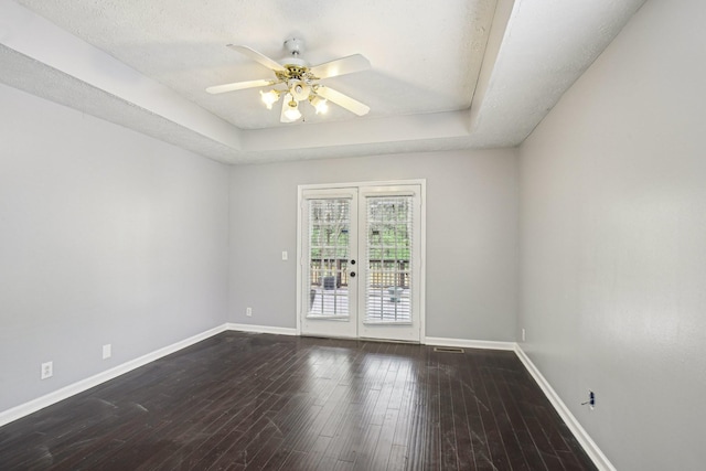 unfurnished room with a raised ceiling, baseboards, ceiling fan, and dark wood finished floors