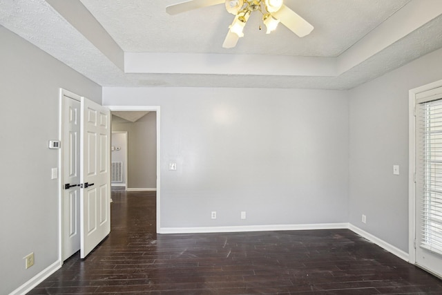 spare room with a textured ceiling, baseboards, ceiling fan, wood finished floors, and a raised ceiling
