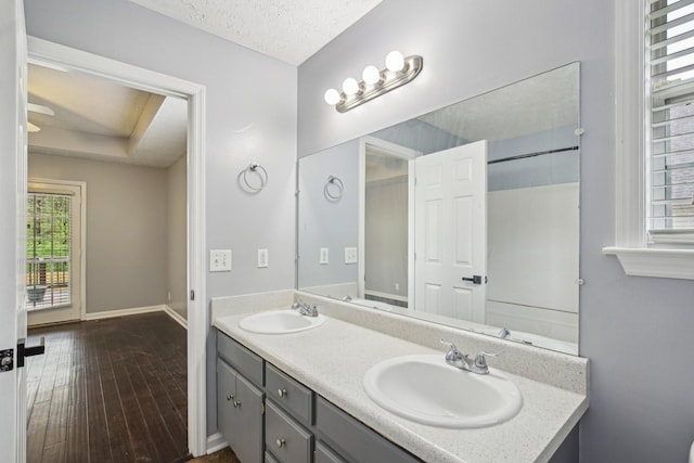 full bathroom featuring double vanity, a textured ceiling, a sink, and wood finished floors