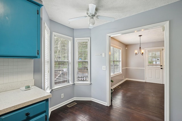 interior space featuring ceiling fan with notable chandelier, a textured ceiling, dark wood finished floors, baseboards, and visible vents