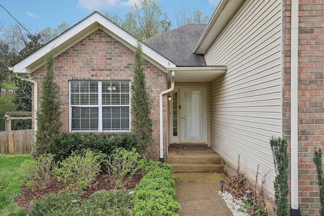 property entrance featuring a shingled roof, fence, and brick siding