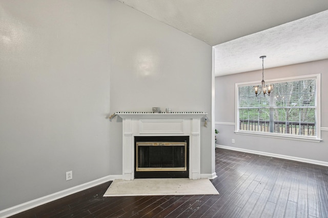 unfurnished living room with an inviting chandelier, dark wood-style flooring, a fireplace with raised hearth, and baseboards