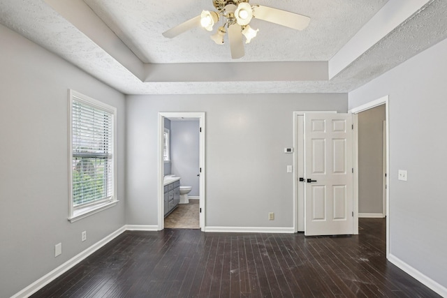 unfurnished bedroom featuring a tray ceiling, baseboards, a textured ceiling, and dark wood-type flooring
