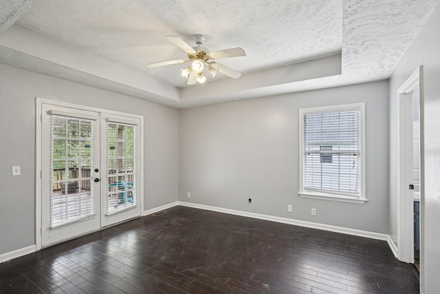 unfurnished room featuring french doors, a tray ceiling, baseboards, and dark wood finished floors