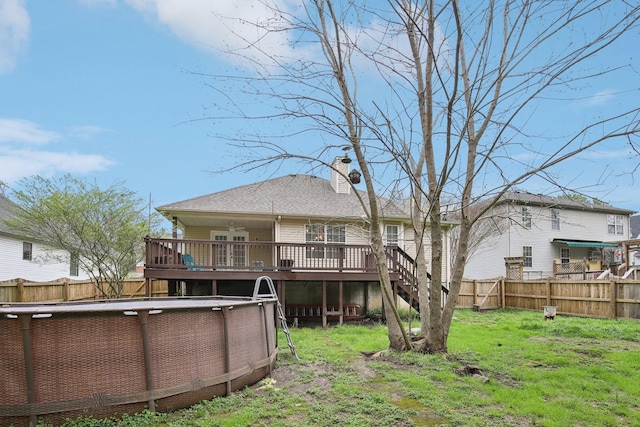 back of house featuring a wooden deck, a chimney, a fenced in pool, a fenced backyard, and a yard