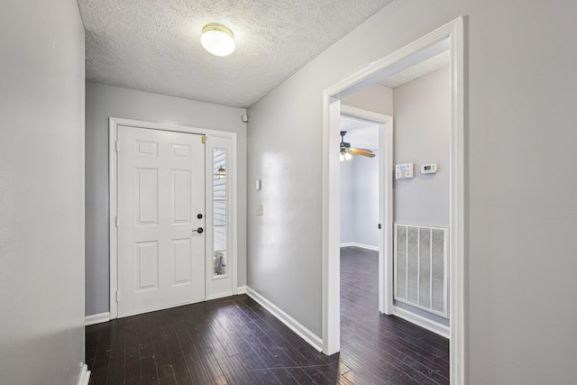 foyer entrance featuring baseboards, visible vents, dark wood-type flooring, and a textured ceiling