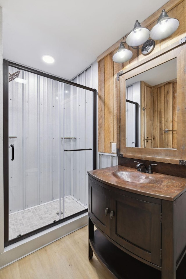 full bath with vanity, wood finished floors, a shower stall, and wood walls