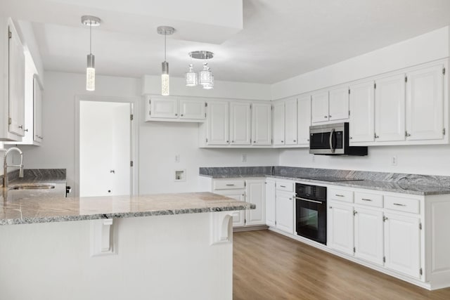 kitchen with light stone countertops, a sink, a peninsula, and black appliances