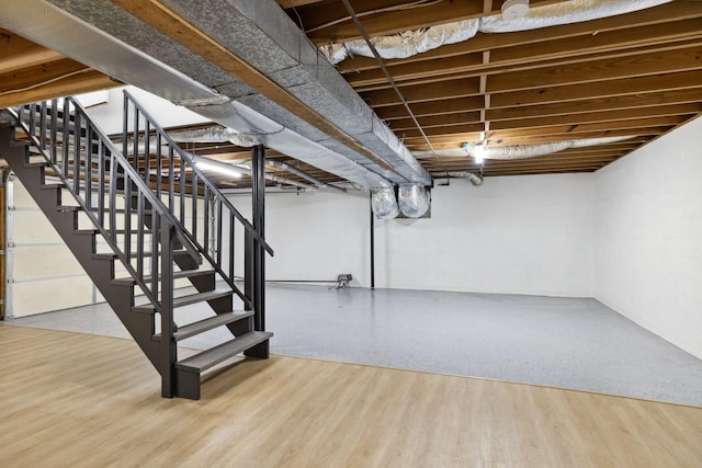finished basement with stairs, concrete block wall, and wood finished floors
