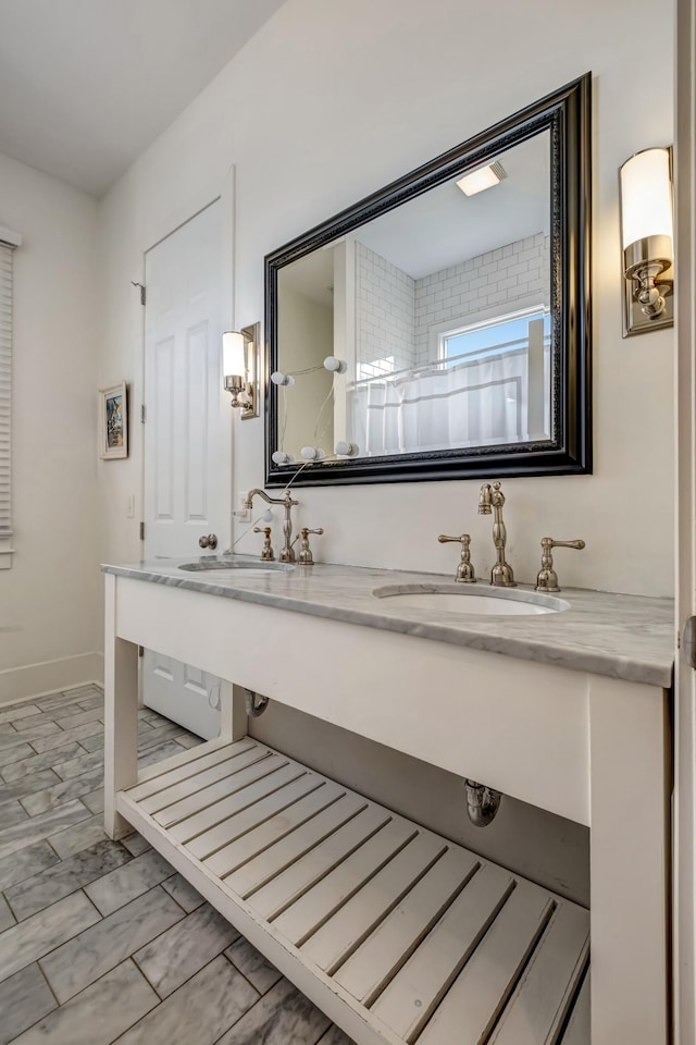 full bath with double vanity, baseboards, and a sink