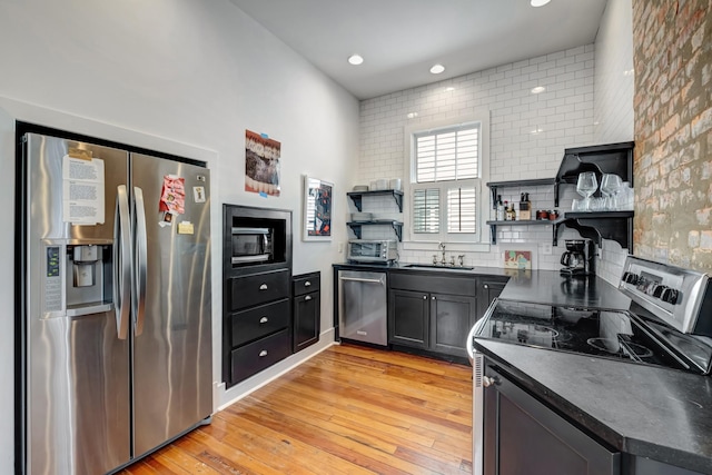 kitchen featuring open shelves, light wood-type flooring, a sink, dark countertops, and appliances with stainless steel finishes