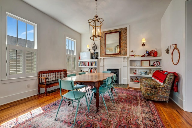 dining room featuring baseboards, a fireplace, wood finished floors, and a chandelier