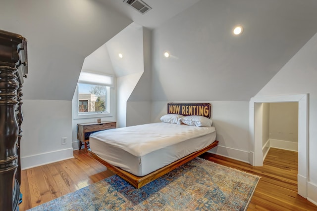 bedroom with baseboards, visible vents, vaulted ceiling, and wood finished floors