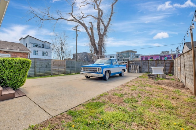 view of parking with fence and concrete driveway