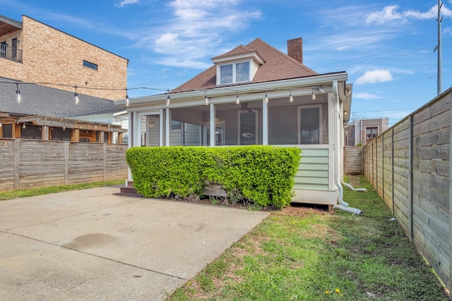 rear view of house featuring a fenced backyard, a sunroom, roof with shingles, and a patio