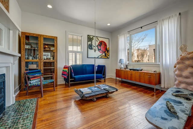 living area with a fireplace with flush hearth, baseboards, recessed lighting, and wood-type flooring