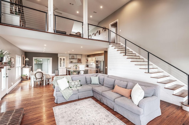 living room with stairs, a towering ceiling, wood finished floors, and recessed lighting