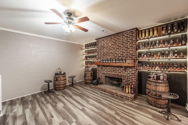 unfurnished living room featuring visible vents, wood finished floors, a ceiling fan, and a brick fireplace