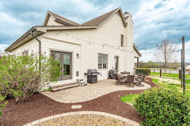 rear view of property featuring a chimney, fence, brick siding, a shingled roof, and a patio