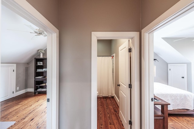 corridor with baseboards, wood finished floors, and vaulted ceiling