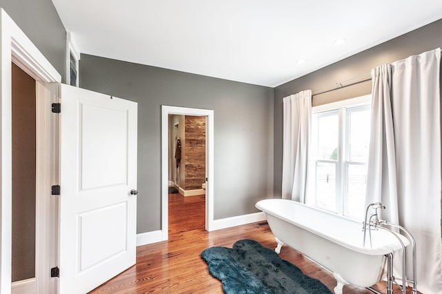 full bath featuring baseboards, a freestanding bath, and wood finished floors