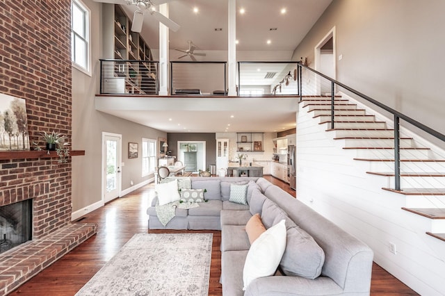 living room with stairway, a high ceiling, a ceiling fan, a fireplace, and wood finished floors