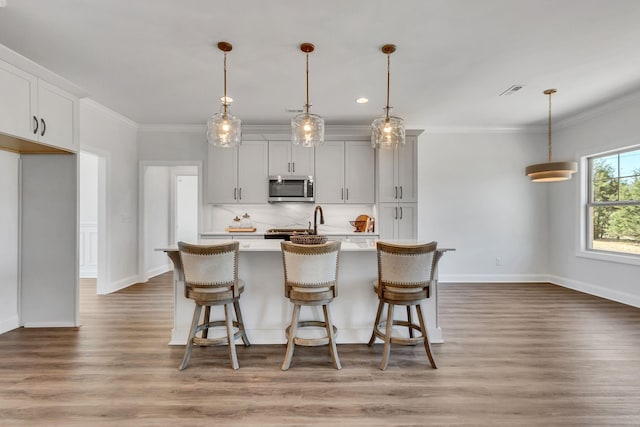 200 Creekside Dr, Lewisburg, TN 37091 - kitchen featuring light countertops, crown molding, stainless steel microwave, decorative backsplash, and a center island with sink
