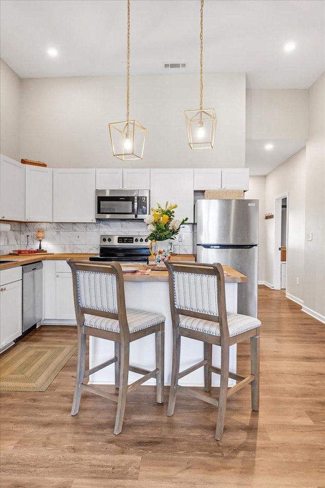 kitchen featuring light wood-style flooring, visible vents, white cabinets, stainless steel appliances, and backsplash